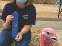 Child wearing mask holding blue ribbon reading "North Carolina State Fair" beside a turkey