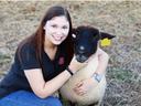Woman crouching outdoors hugging a black-faced sheep with a yellow ear tag