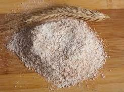 Pile of whole wheat flour on a wooden board with a wheat stalk