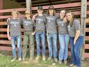 Six teens in matching "Northwood FFA" shirts standing arm-in-arm before a red livestock pen