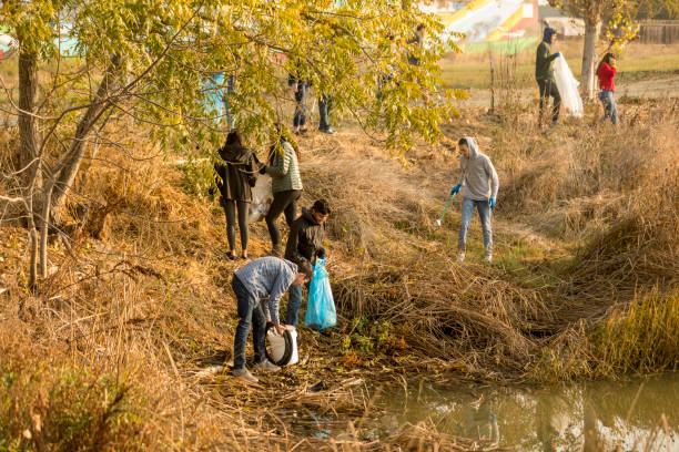 Volunteers picking up litter along a grassy pond bank with trash bags