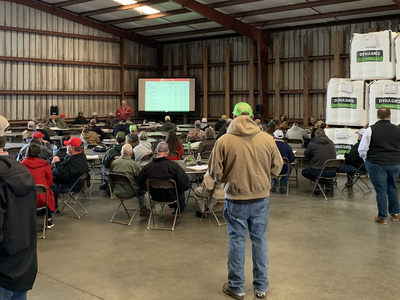 Indoor meeting in a warehouse with attendees seated facing a presenter and projection screen