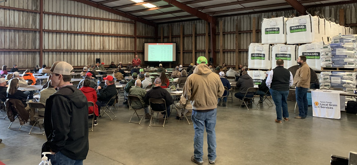 Indoor meeting in a warehouse with attendees seated facing a presenter and projection screen