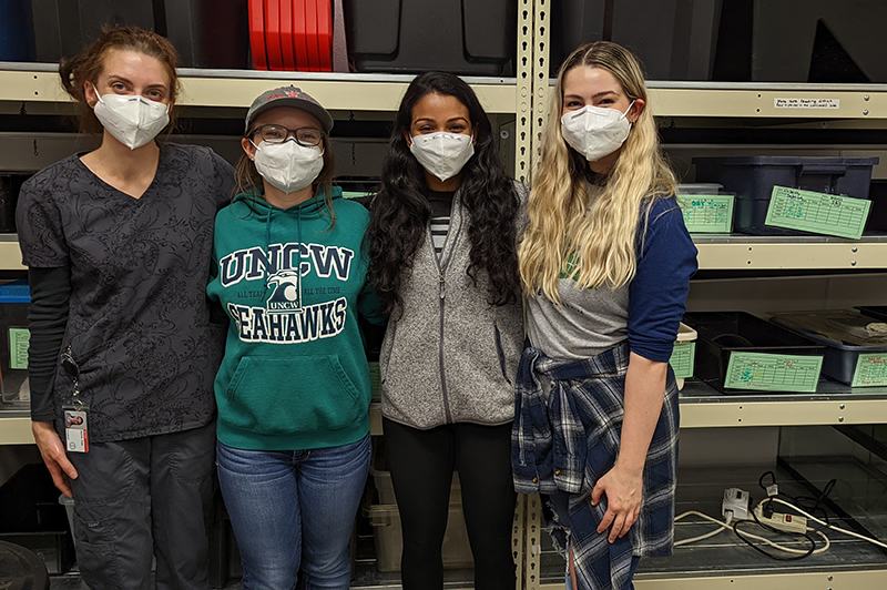 Four masked women standing together in front of storage shelves