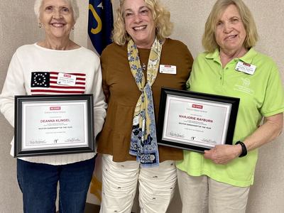 Three women standing; two hold framed certificates: "Deanna Klingel" and "Marjorie Rayburn, Master Gardener of the Year."