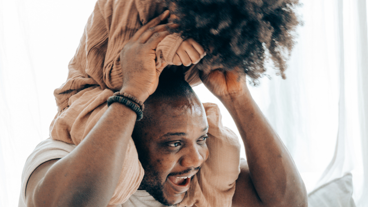 Man holding a child on his shoulders while the child grips his head
