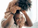 Man carrying child on his shoulders indoors, child seated facing forward