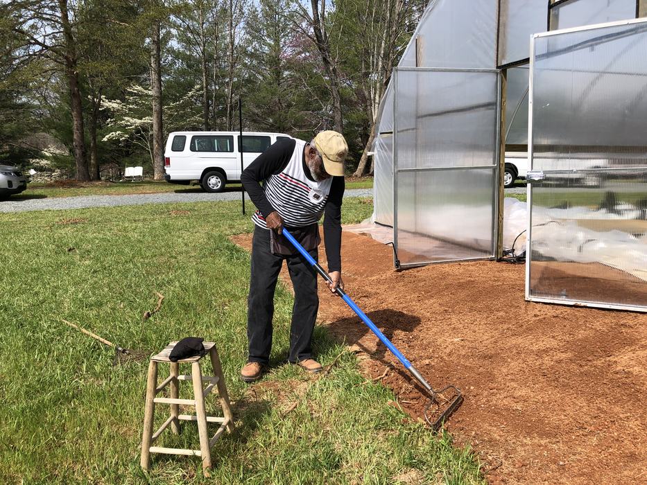 Person raking soil along the entrance of a plastic greenhouse