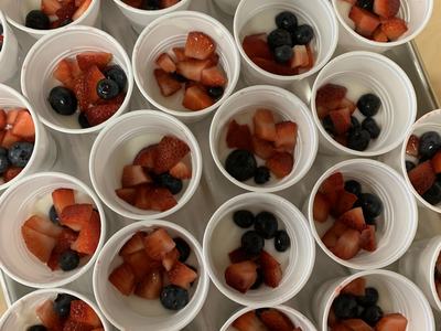 White plastic cups filled with yogurt and topped with diced strawberries and blueberries