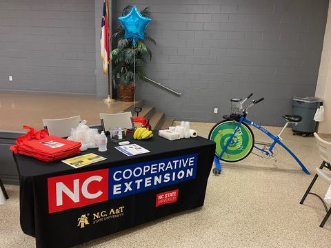 NC Cooperative Extension table with brochures, bananas, cups, and a blender bike beside it.