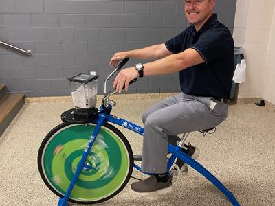 Person pedaling a stationary blender bike with a green spinning front wheel
