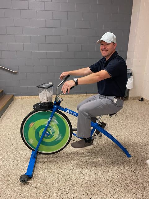Person pedaling a stationary blender bike with a green spinning front wheel