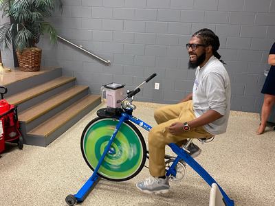 Man pedaling a stationary blender bike indoors with a blender jar mounted on the handlebars
