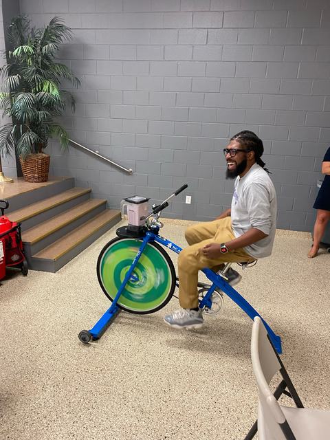Man pedaling a stationary blender bike indoors with a blender jar mounted on the handlebars