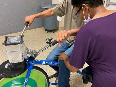 Two people operating a stationary blender bike labeled "N.C. A&T Cooperative Extension" and "HEALTHY"