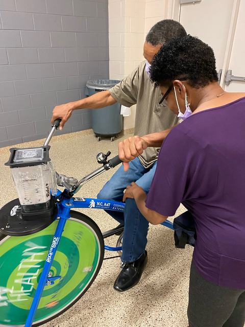 Two people operating a stationary blender bike labeled "N.C. A&T Cooperative Extension" and "HEALTHY"