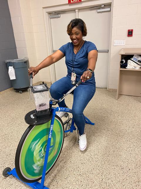 Woman pedaling stationary blender bike labeled "Rock the Bike" beneath an EXIT sign