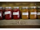 Row of mason jars labeled "Strawberry Jam" and "Pumpkin Butter" on wooden shelf