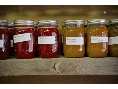 Row of mason jars labeled "Strawberry Jam" and "Pumpkin Butter" on wooden shelf