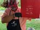Person wearing mask and apron holds red bag reading "Enjoy local foods, visit local farms."
