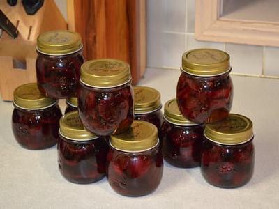 Nine small glass jars with gold lids filled with dark red preserved cherries on countertop