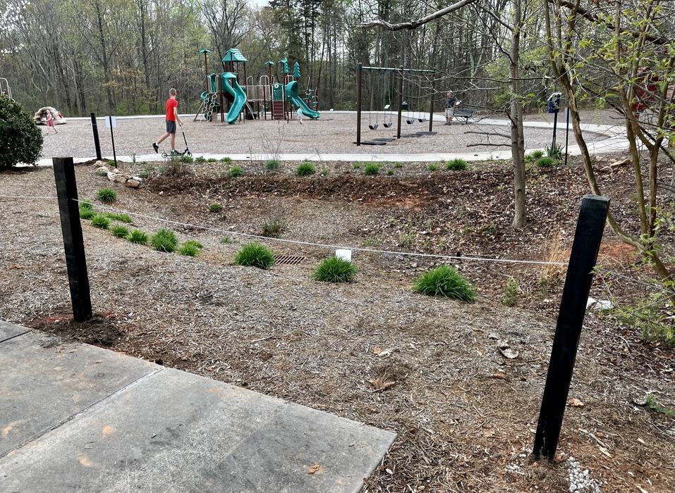 Playground with green slides and swings; boy in red shirt riding a scooter