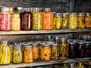 Glass jars of pickled and preserved vegetables arranged on wooden pantry shelves