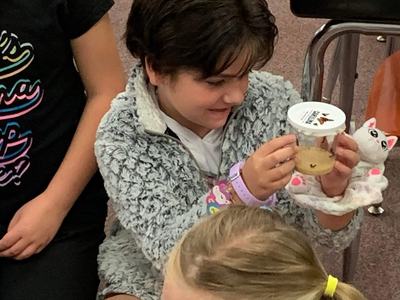 Child seated on floor holding a clear plastic cup containing a small larva or insect