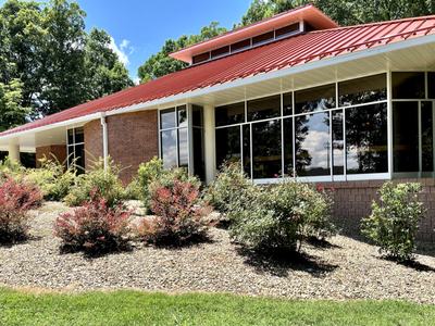 Single-story brick building with red metal roof and landscaped shrub beds
