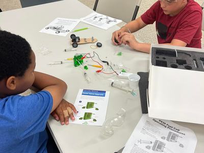 Two boys assembling a small PEM fuel cell car kit at a table with instructions