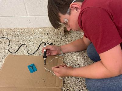 Person wearing safety glasses using a soldering iron on a wire over cardboard