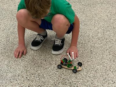 Boy crouching on speckled floor adjusting a small homemade toy car