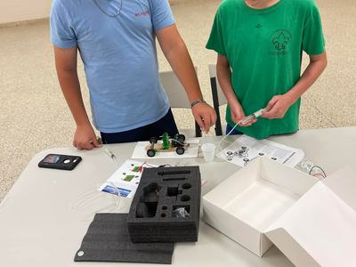 Two boys assembling a small wheeled model car on a table with parts and packaging