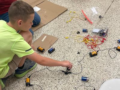 Child kneeling on floor connecting batteries and wires for a circuit project