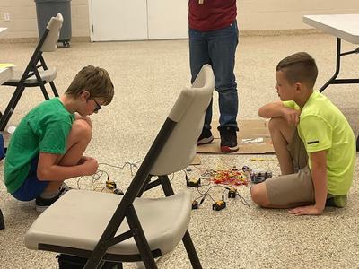 Three boys in a room assembling electronic circuits and wiring on the floor.