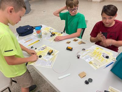 Three boys at a table assembling battery-powered circuit kits with wires and worksheets