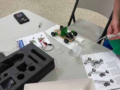 Small green model car on table with tubing and syringe, instruction sheet reading "Assembly Procedure"