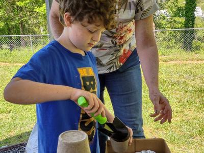 A child fills a small vessel with soil.