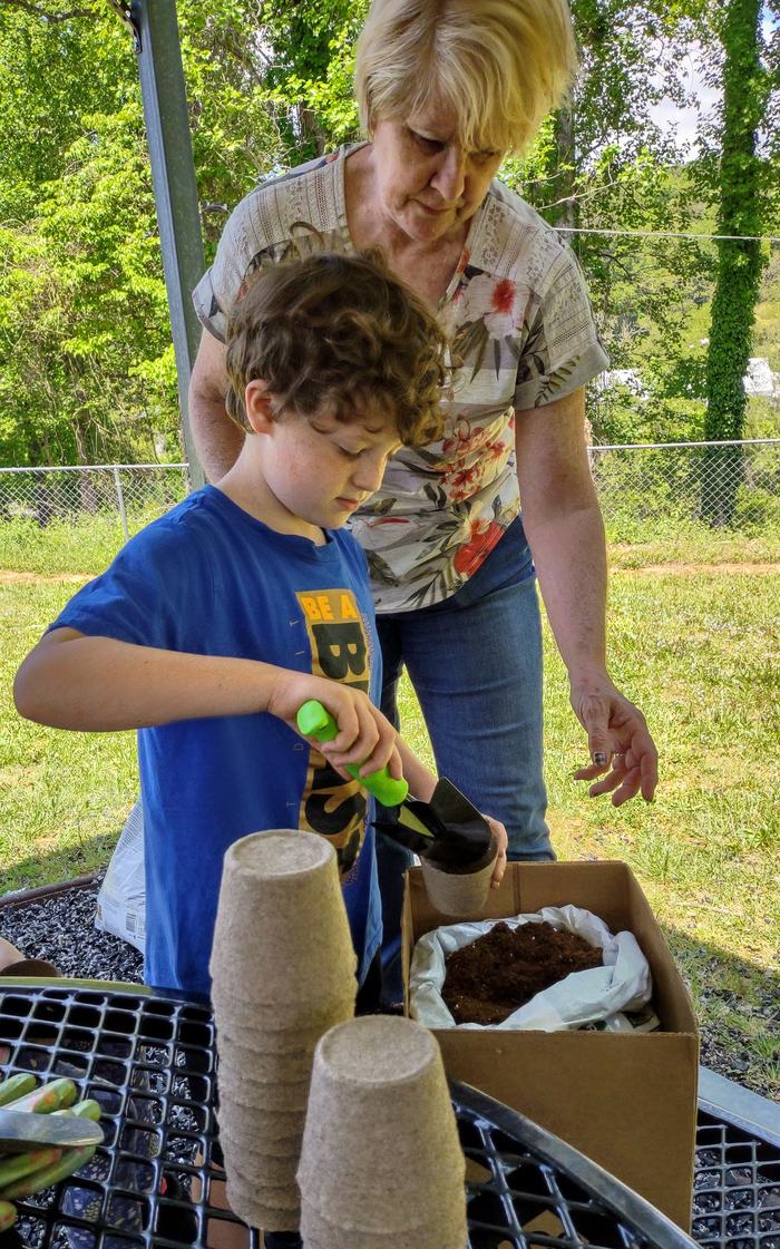 A child fills a small vessel with soil.
