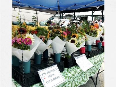 Market table of wrapped bouquets under canopy; sign: "$10 BOUQUETS FRESH CUT FLOWERS"