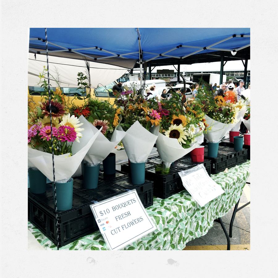 Bouquets of fresh cut flowers for sale on a table under a blue tent.