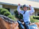 Child wearing helmet on horse holding two red-white-blue medal ribbons