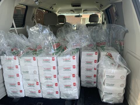 SUV cargo area filled with stacked Krispy Kreme fundraising donut boxes and plastic bags