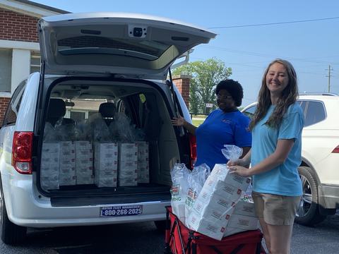 Two people loading boxes of Krispy Kreme doughnuts into a minivan trunk