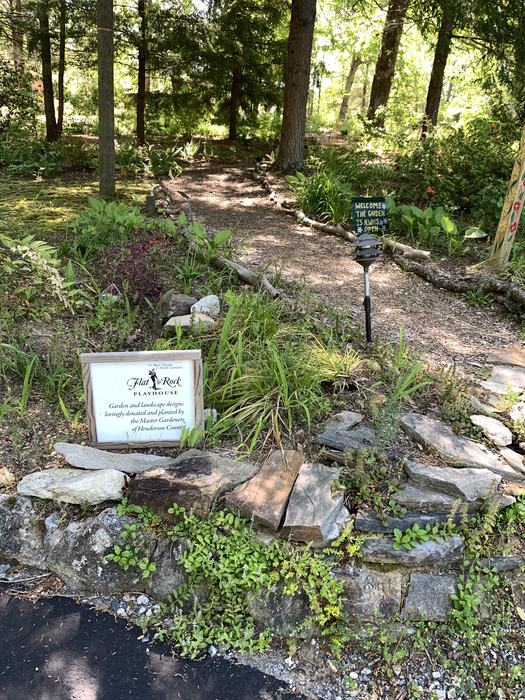A path through a garden of low green plants. There is a white sign at ground level.
