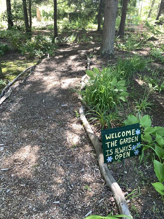 A garden sign displays "Welcome, the Garden is always open." beside a path.