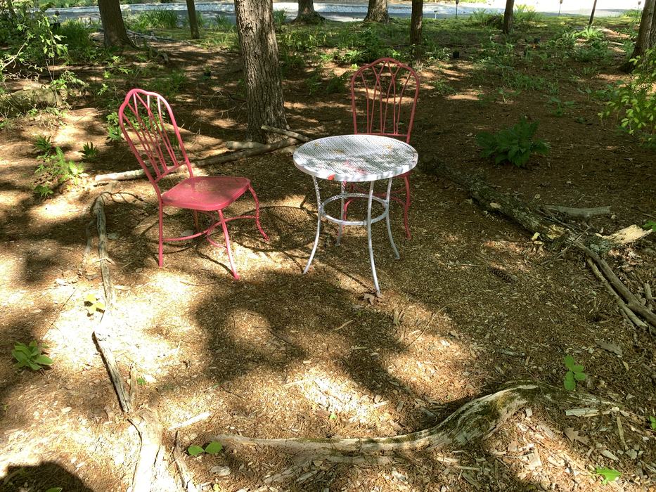 Two red chairs and a white table in a shaded area. 
