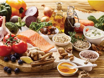 Assorted healthy foods on wooden board: salmon, tomatoes, vegetables, nuts, seeds, oils