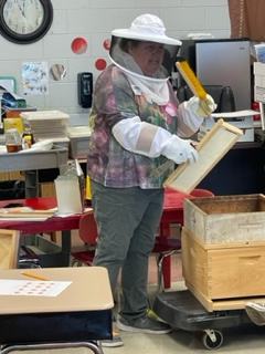 A woman in a classroom demonstrating beekeepers equipment.
