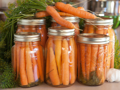 Mason jars filled with pickled carrots and dill, fresh carrots resting on top